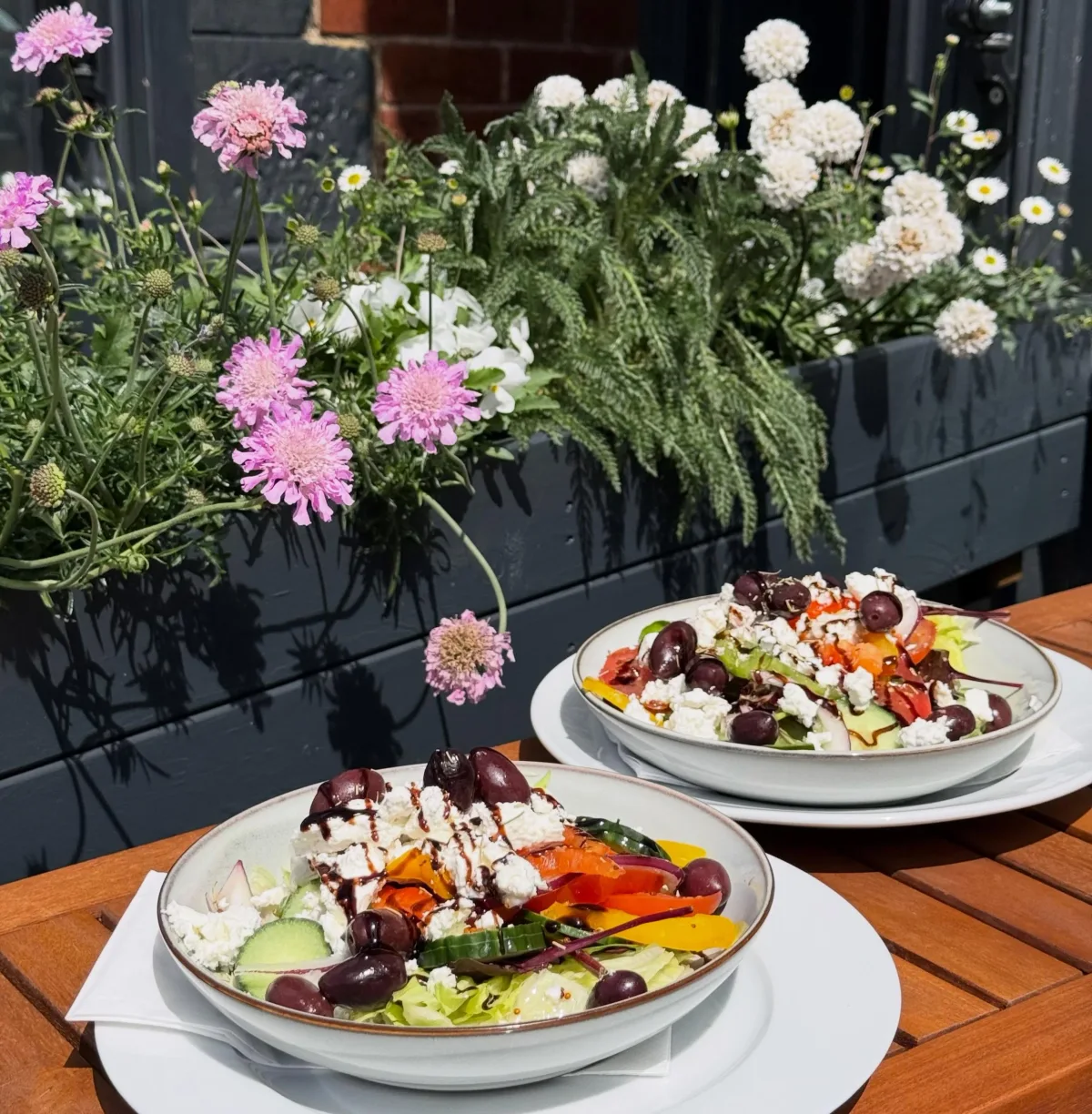 Two fresh salads on the outdoor table beside Kitchen91’s flower planters